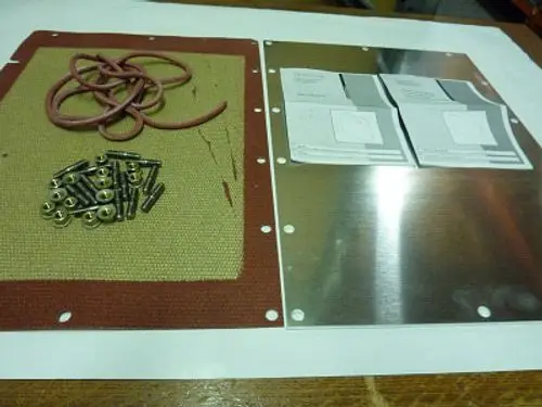 Inspektiondeckel mit roten Dichtungen, Schrauben und Montageanleitung, verwendet für Wärmetauscher. Teile in der Nähe, möglicherweise für Remeha Produkte.